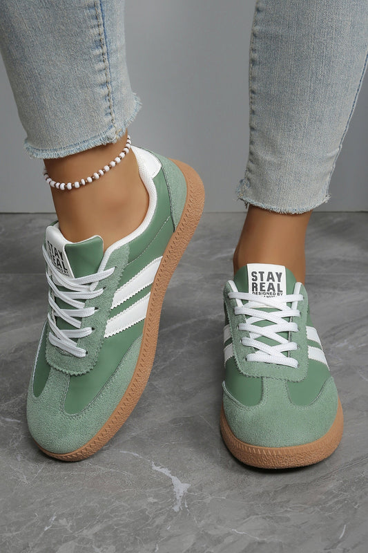 Green sneakers with white laces worn with light blue jeans on a gray floor.