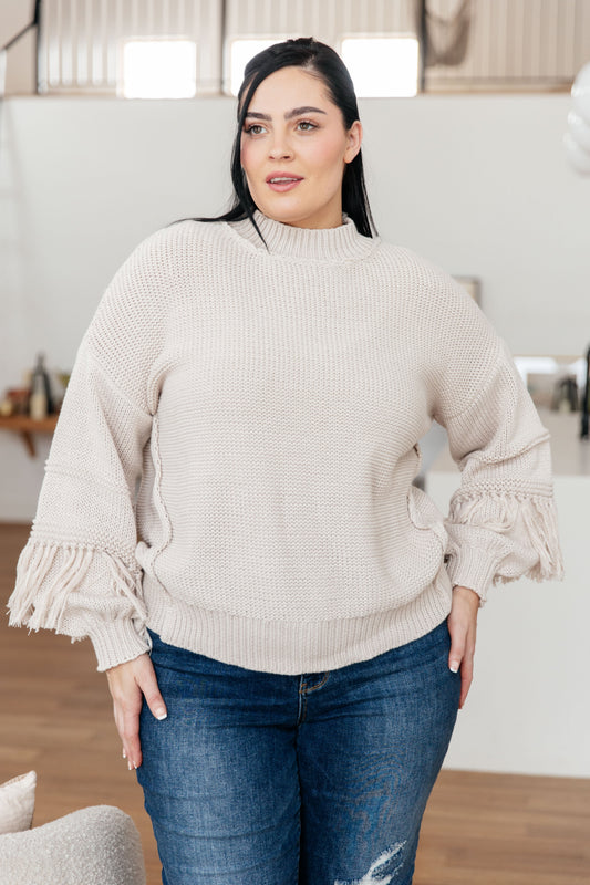 Woman wearing a beige sweater with ruffled sleeves in an indoor setting