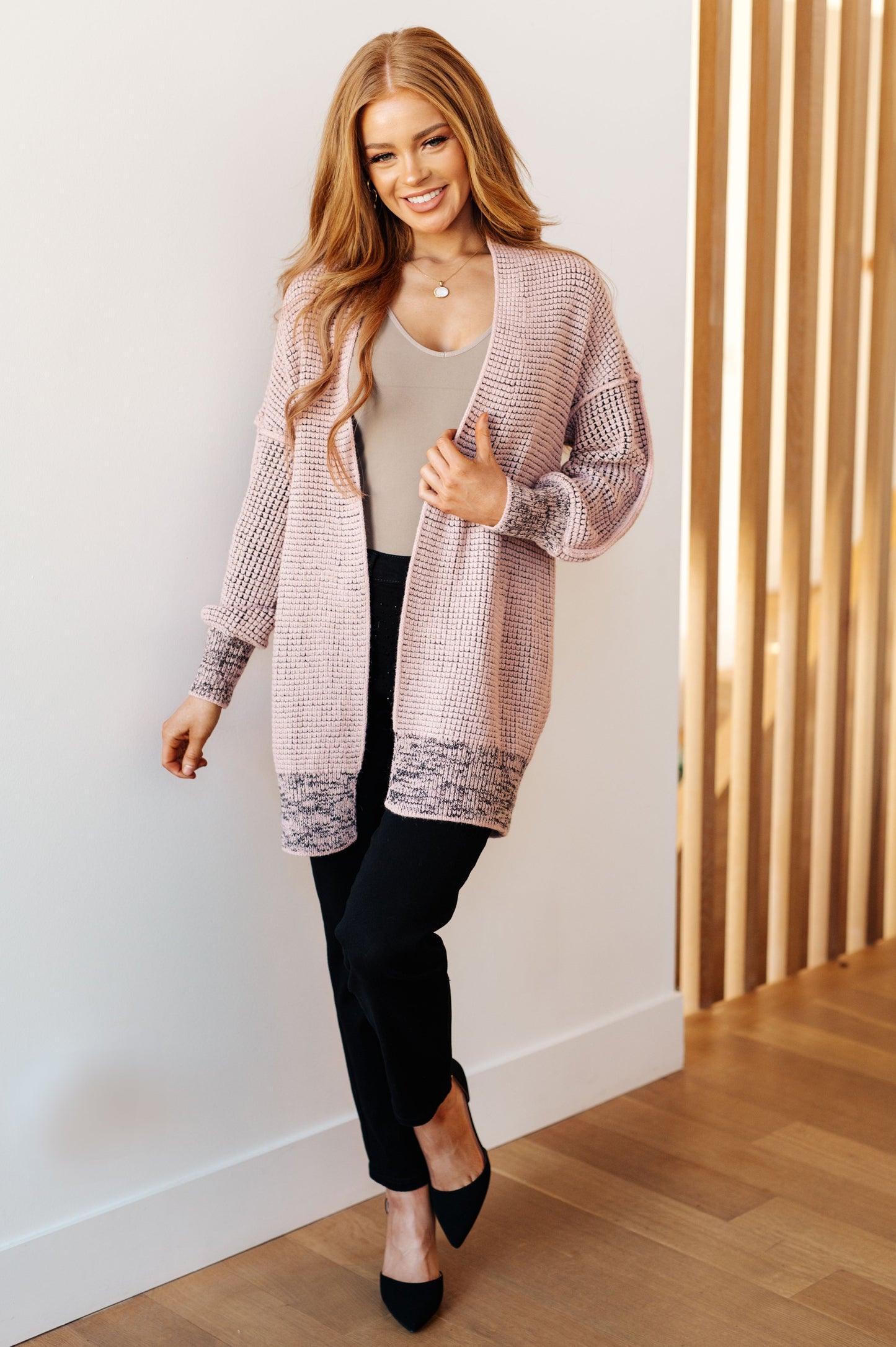 Woman wearing a long, patterned cardigan in an indoor setting.