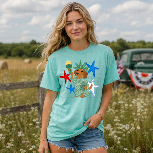 Comfort Colors Chalky Mint graphic tee featuring a patriotic dachshund dressed as the Statue of Liberty with red, white, and blue stars and optional Weenie Proud to Be American wording.