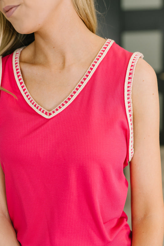 Close-up of a pink sleeveless top with decorative trim on a blurred background