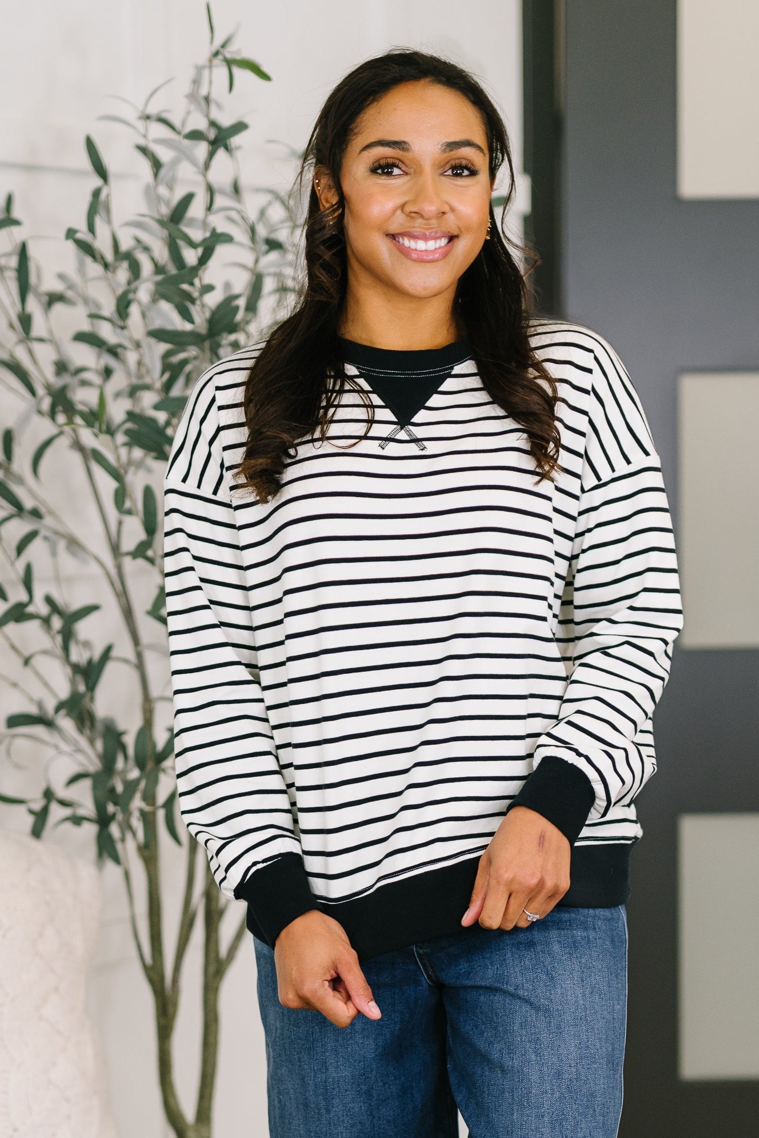 Woman wearing a black and white striped sweater with blue jeans indoors.