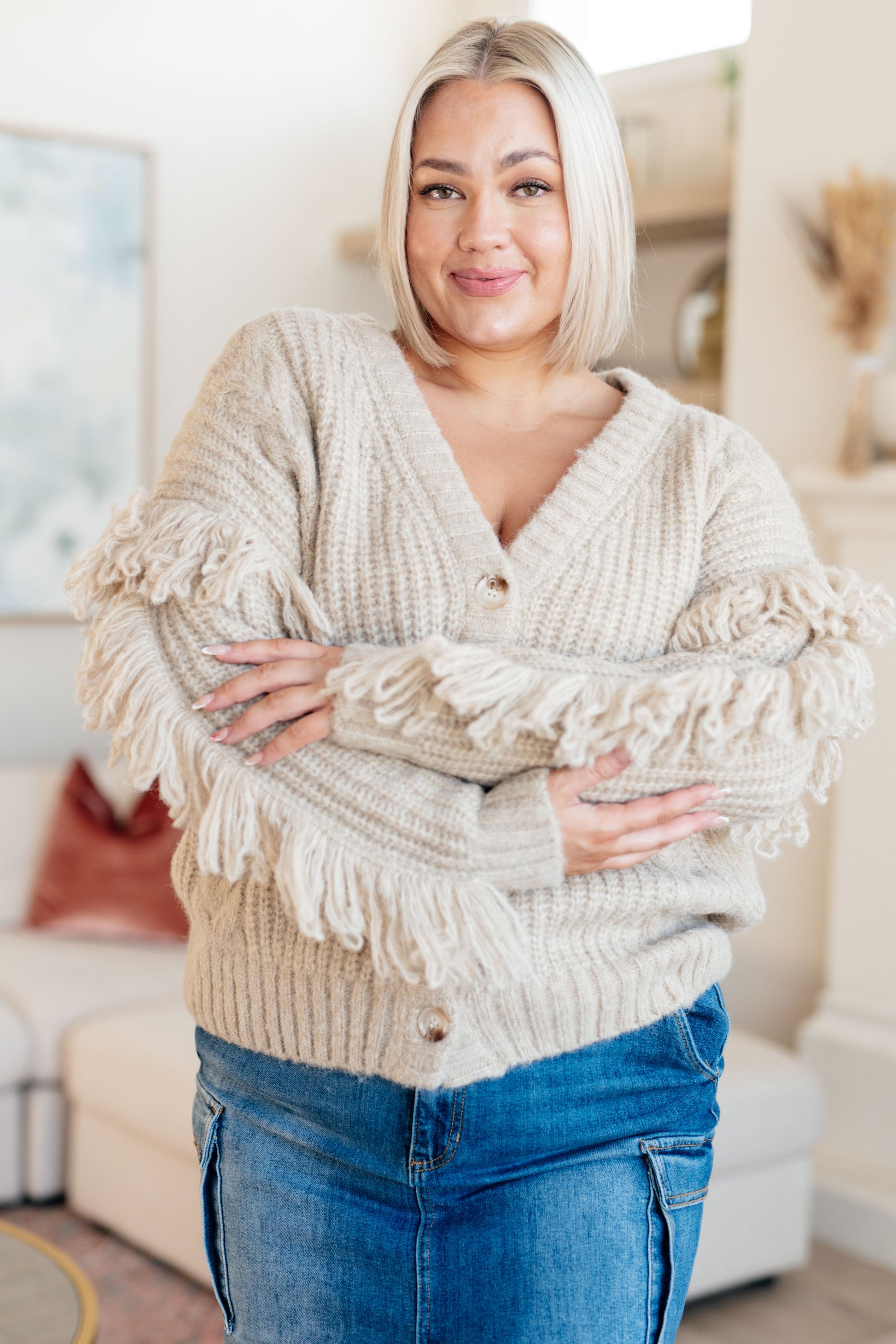 Woman wearing a beige knitted sweater with tassels in a living room setting