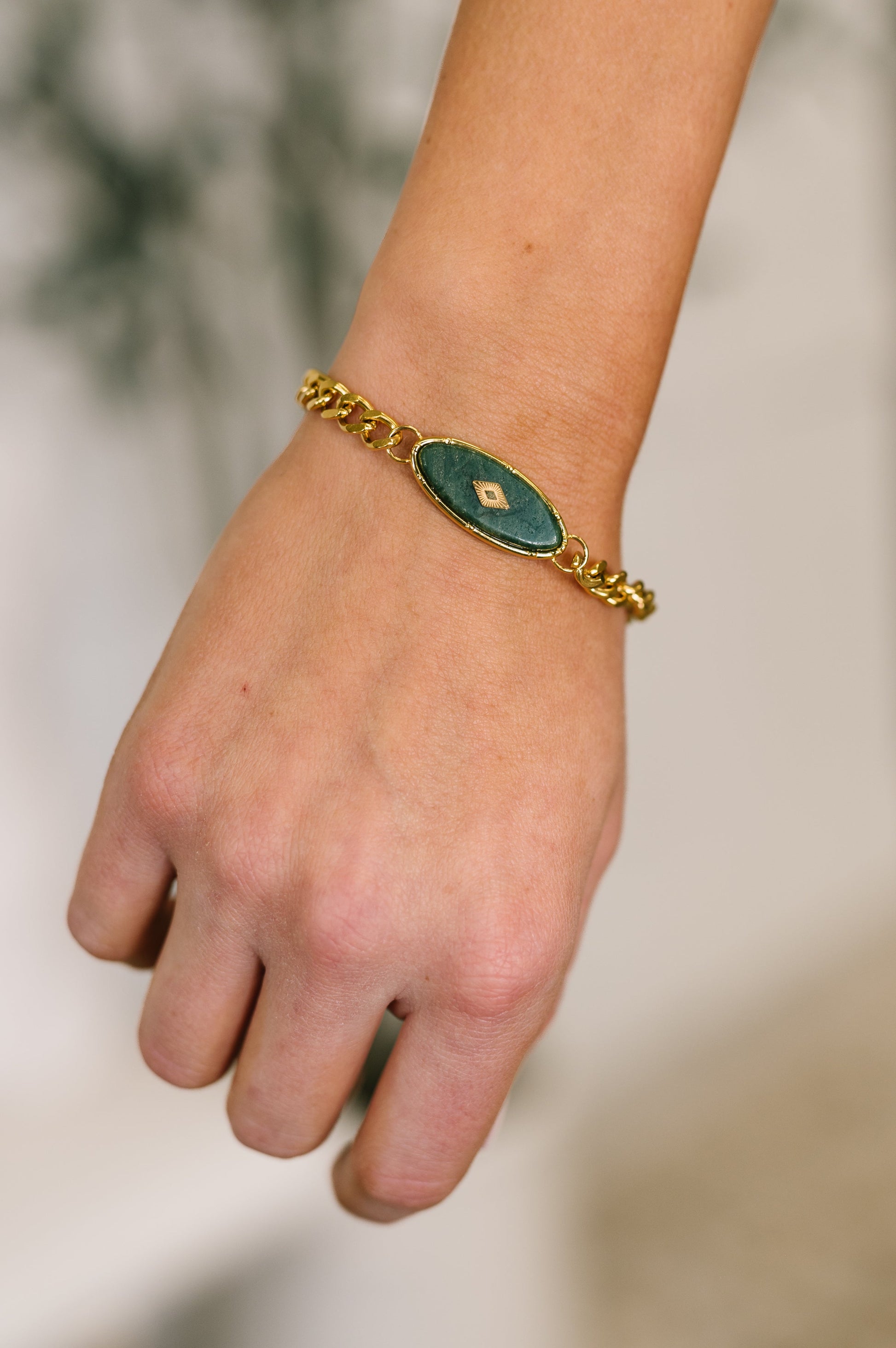 Hand wearing a gold bracelet with a green gemstone on a blurred background