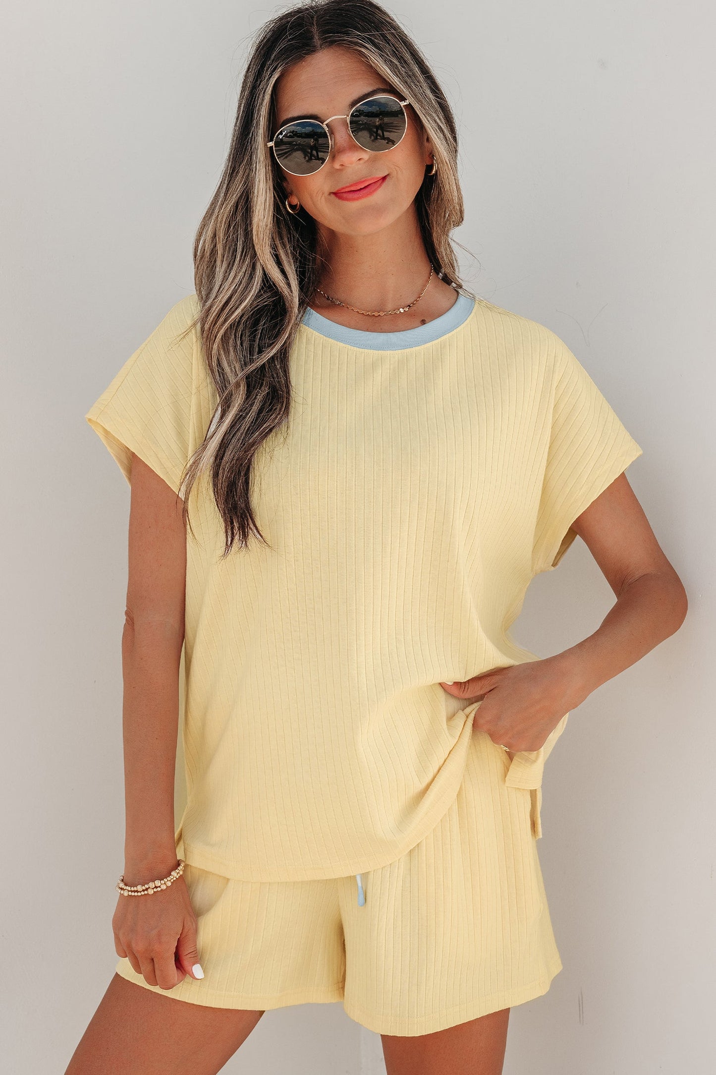 Woman wearing a yellow outfit with sunglasses against a plain background