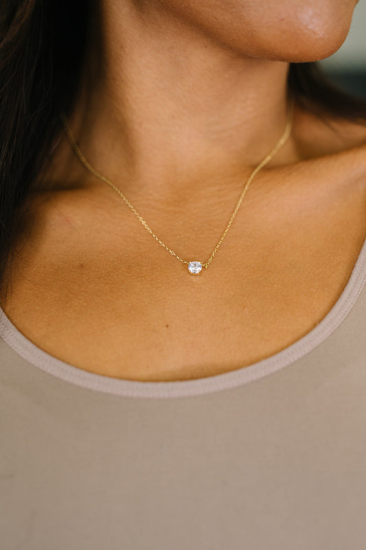 Gold necklace with a blue gemstone on a person wearing a beige top.