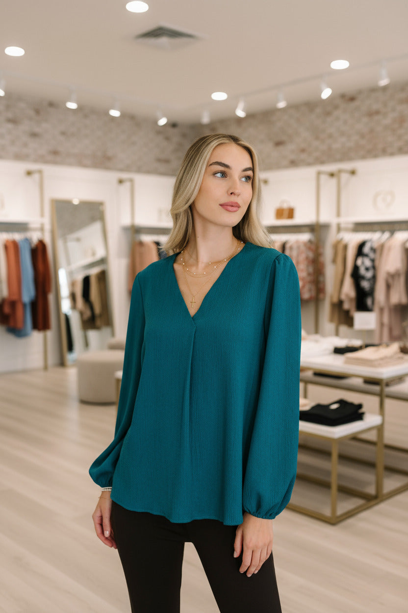 Woman wearing a teal blouse with long sleeves in an indoor setting
