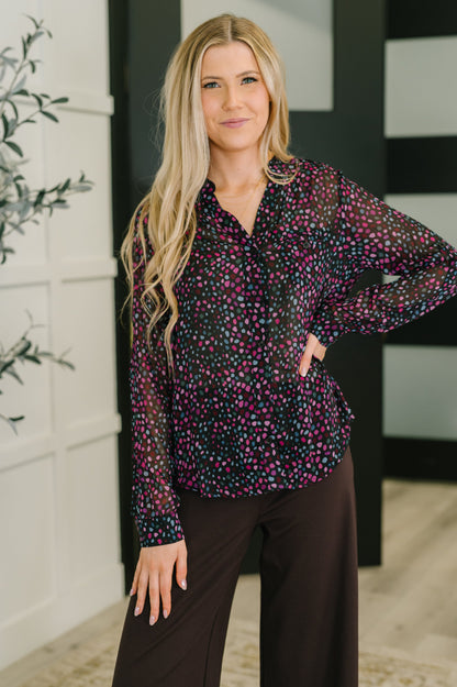 Woman wearing a patterned blouse and dark pants indoors.