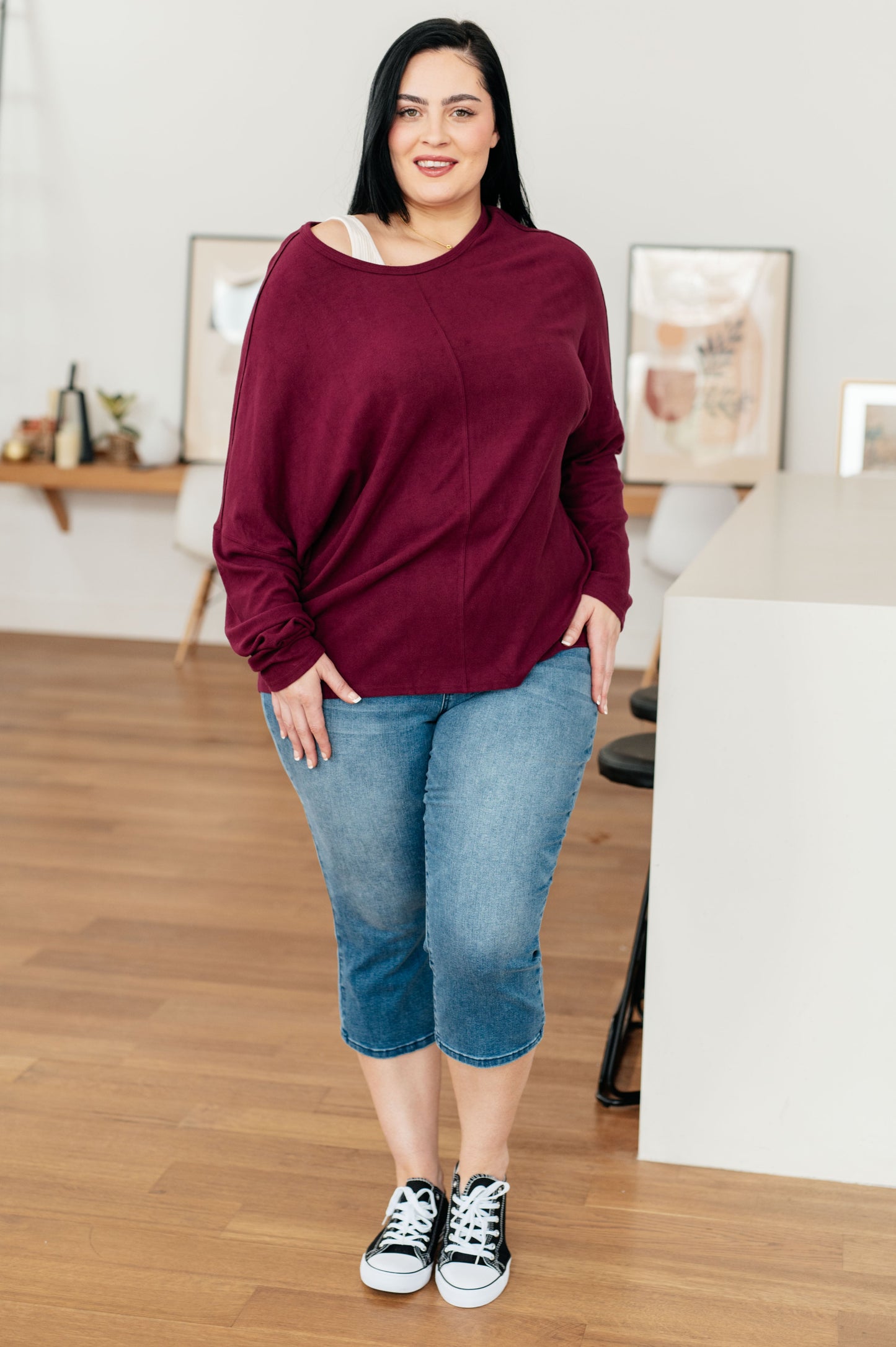 Woman wearing a maroon sweater and blue jeans indoors.