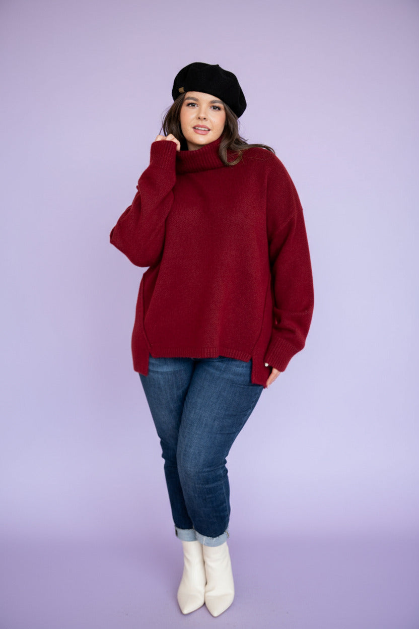 Woman wearing a red sweater and blue jeans in a living room setting.