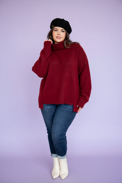 Woman wearing a red sweater and blue jeans in a living room setting.