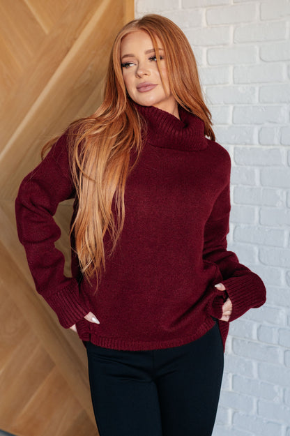 Woman wearing a burgundy sweater against a white brick wall.