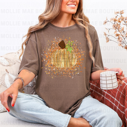 Woman wearing a brown t-shirt with a pumpkin graphic, sitting on a couch holding a mug.