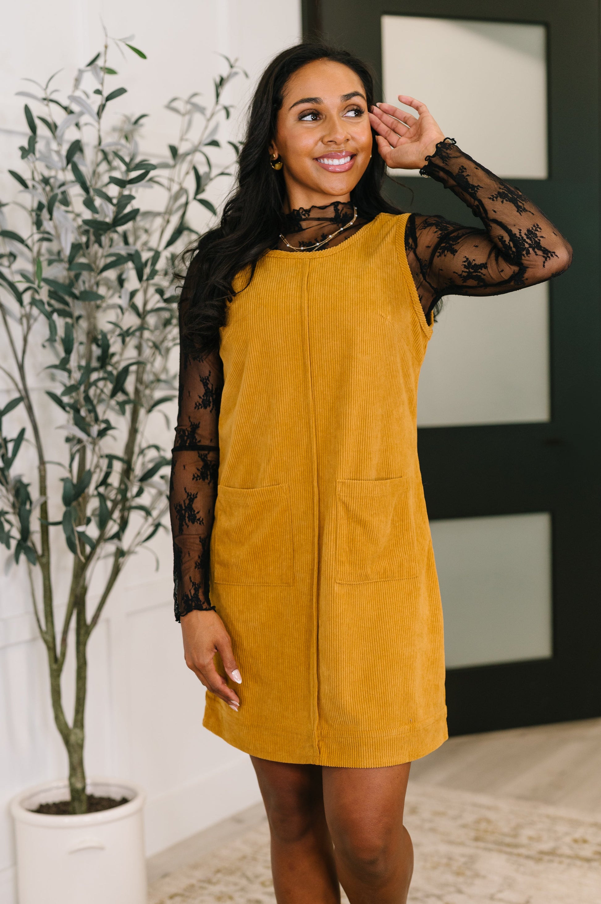 Woman wearing a mustard yellow dress with sheer sleeves indoors.