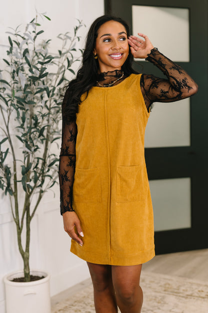 Woman wearing a mustard yellow dress with sheer sleeves indoors.