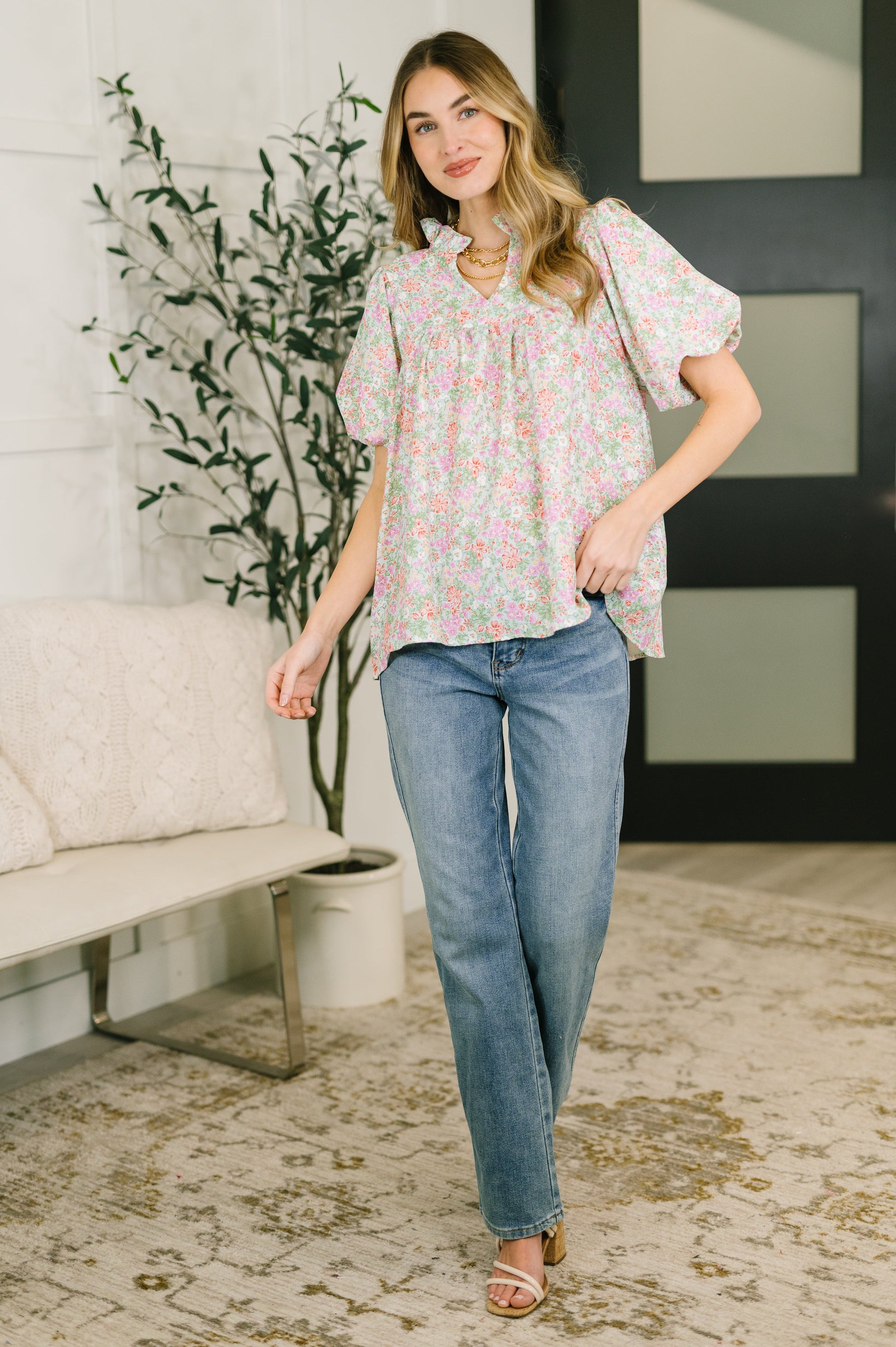 Woman wearing a floral blouse and blue jeans standing in a living room.