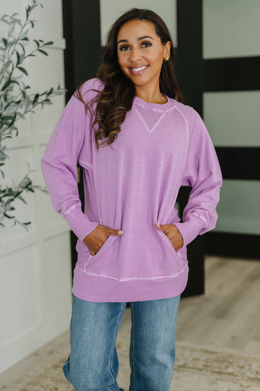 Woman wearing a purple sweatshirt and blue jeans standing indoors.