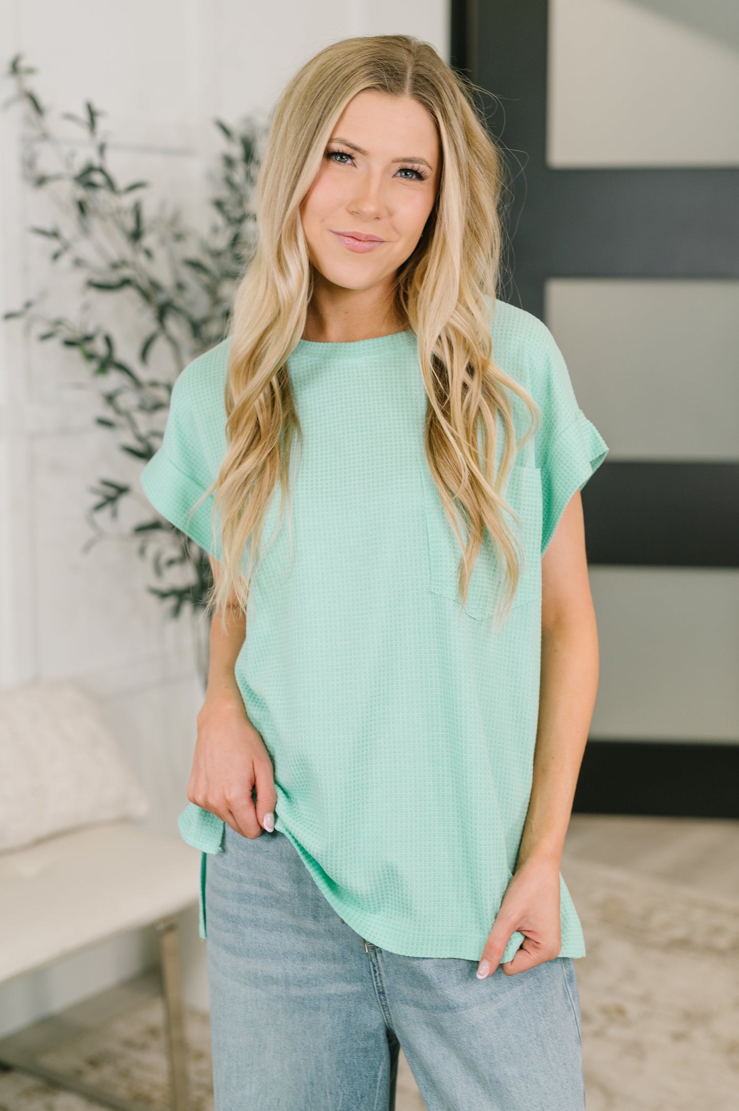 Woman wearing a mint green top and blue jeans indoors.