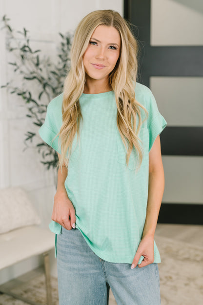Woman wearing a mint green top and blue jeans indoors.