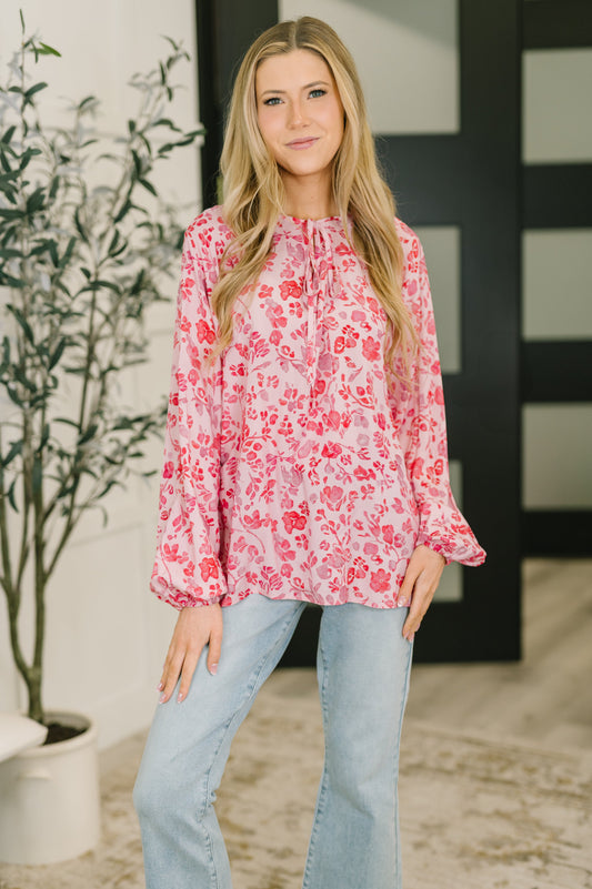 Woman wearing a red floral blouse and light blue jeans standing indoors.