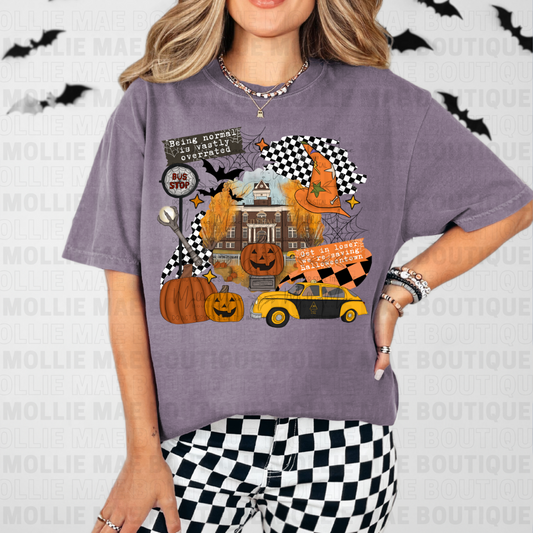 Woman wearing Comfort Colors wine tee with Halloweentown spooky collage design featuring pumpkins, bats, and checkered accents.