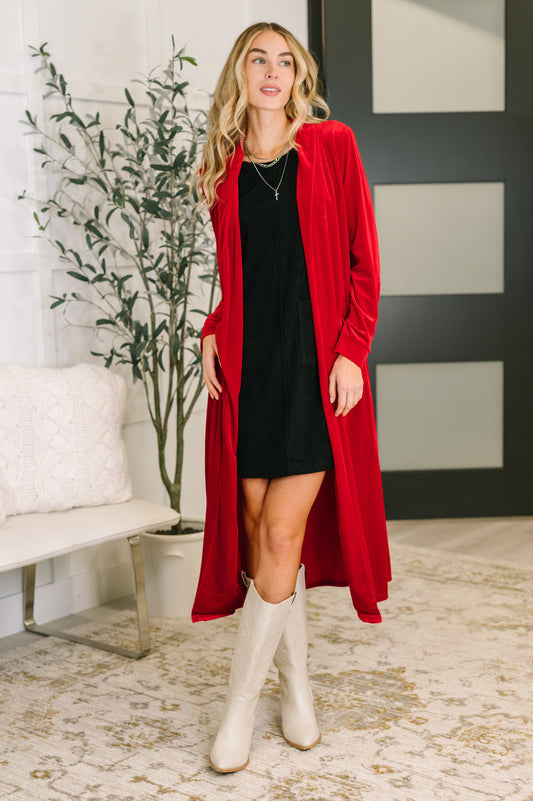 Woman wearing a red cardigan, black dress, and white boots in an indoor setting.