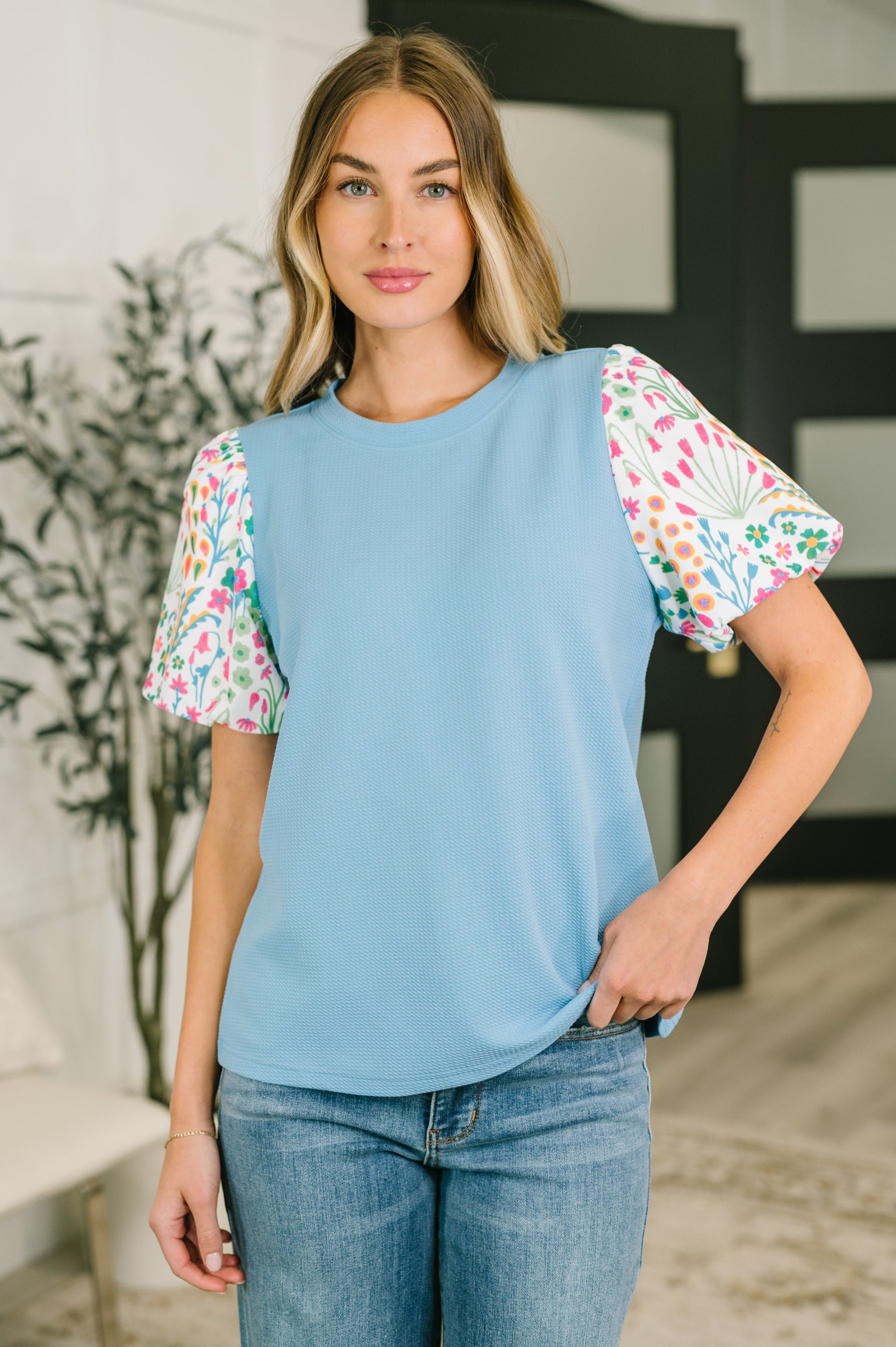Woman wearing a blue top with floral sleeves in an indoor setting