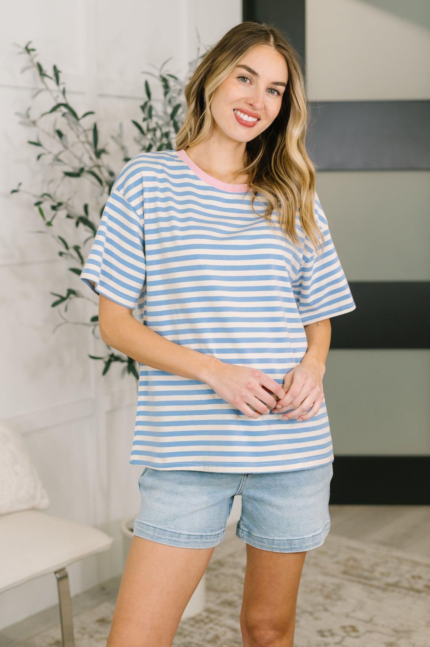 Woman wearing a blue and white striped shirt and denim shorts indoors.