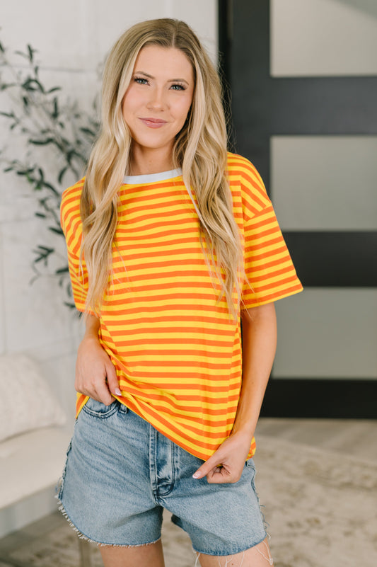 Woman wearing a yellow and orange striped shirt and denim shorts indoors.