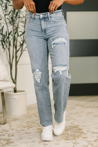Person wearing light blue ripped jeans and white sneakers in an indoor setting.