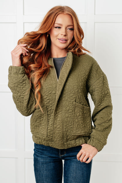 Woman wearing a green quilted jacket against a white tiled wall