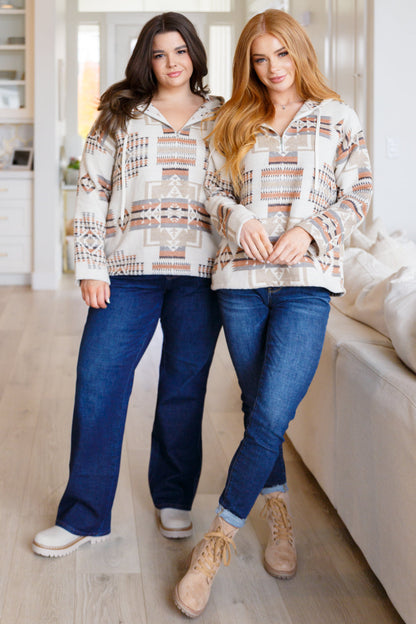 Two women wearing matching patterned hoodies and blue jeans indoors.
