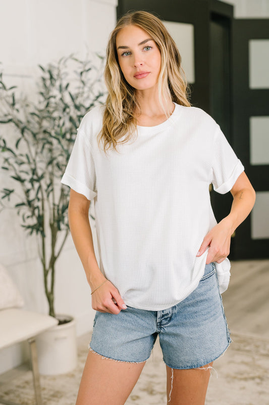 Woman wearing a white t-shirt and denim shorts standing indoors.