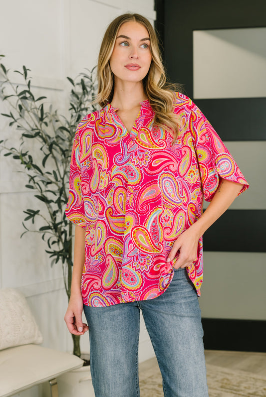 Woman wearing a bright pink paisley shirt in an indoor setting