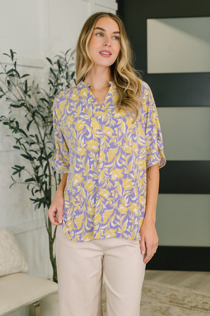 Woman wearing a yellow and purple patterned blouse in an indoor setting.