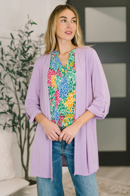 Woman wearing a colorful floral blouse under a light purple cardigan in a home setting.