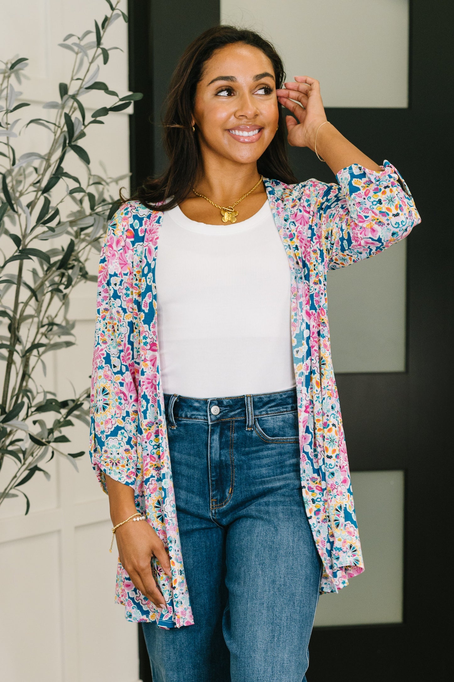 Woman wearing a colorful floral kimono over a white top and blue jeans, standing indoors.