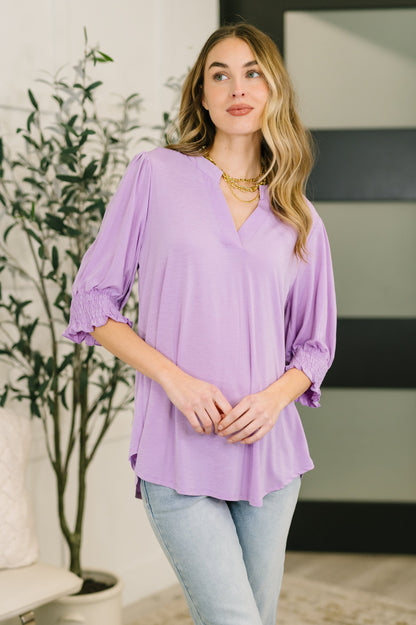 Woman wearing a purple blouse and light blue jeans indoors.