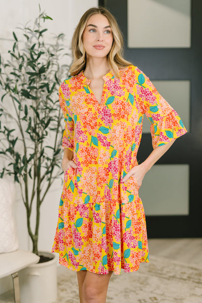 Woman wearing a colorful floral dress in a room with a plant and abstract art on the wall.