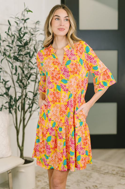 Woman wearing a colorful floral dress in a room with a plant and abstract art on the wall.