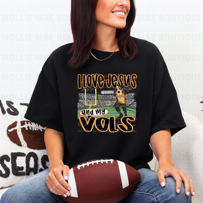 Woman wearing black Gildan tee with “I Love Jesus and My Vols” graphic design, holding football.
