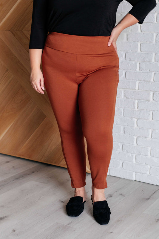 Person wearing rust-colored pants and black shoes against a white brick wall.