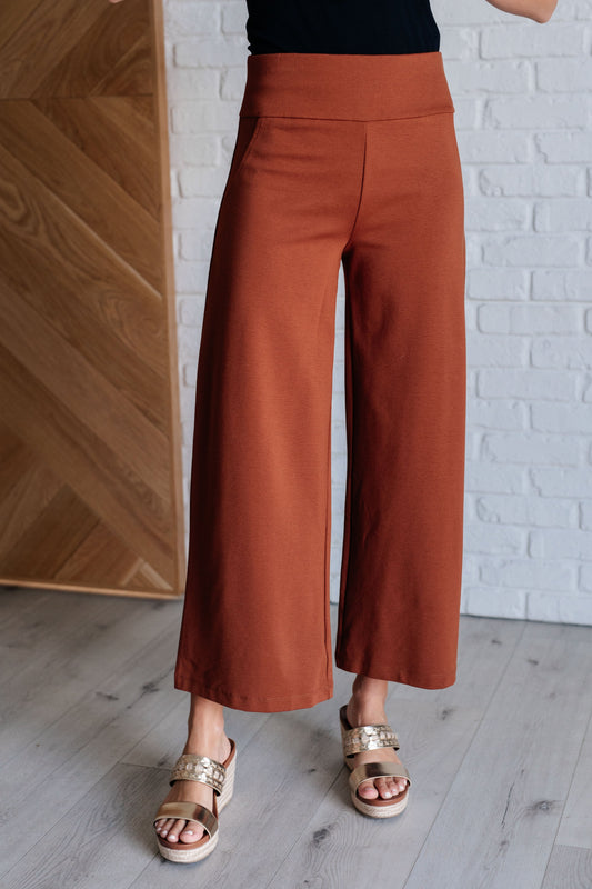 Person wearing rust-colored wide-leg pants against a white brick wall.