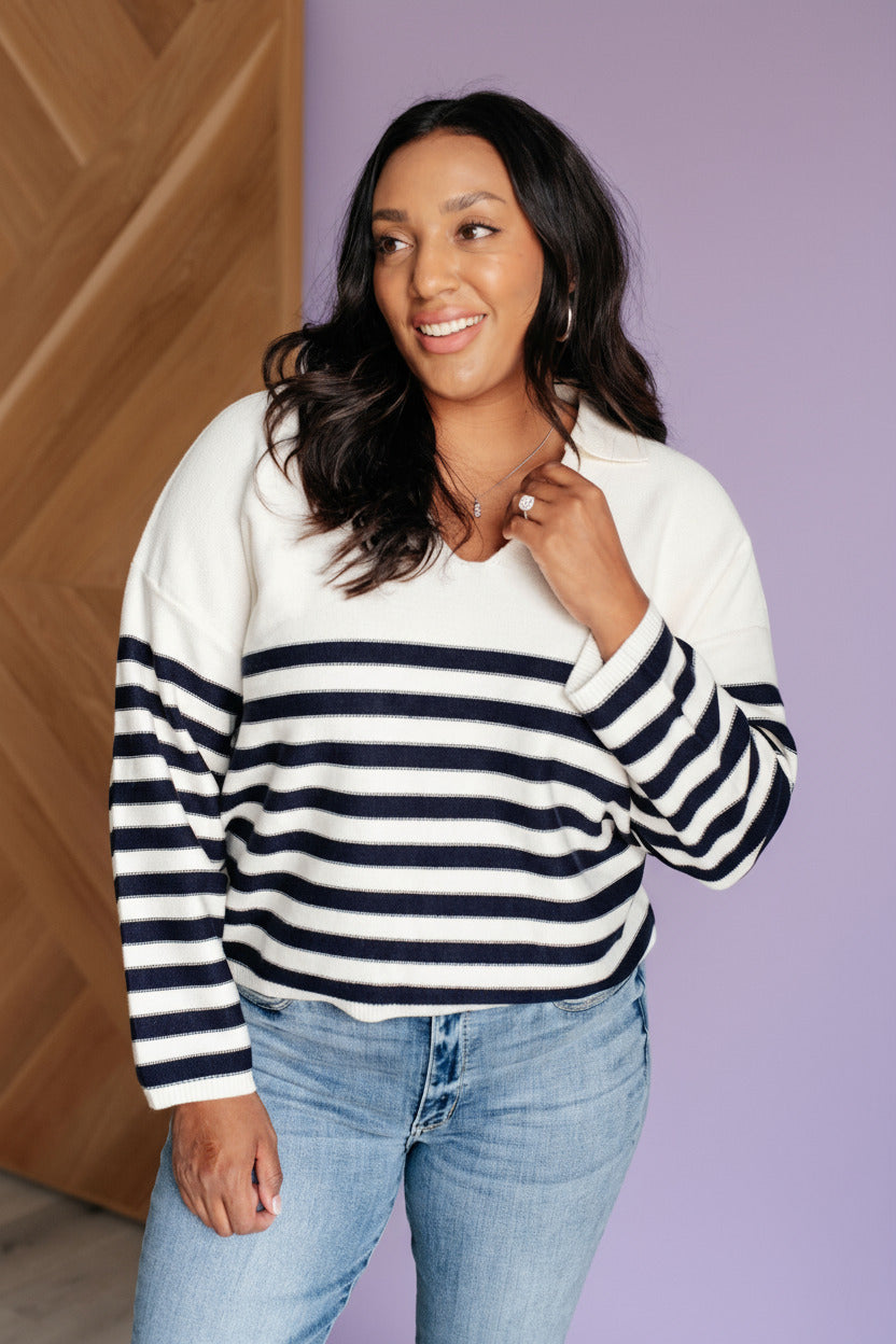 Woman wearing a striped sweater and jeans against a white brick wall.