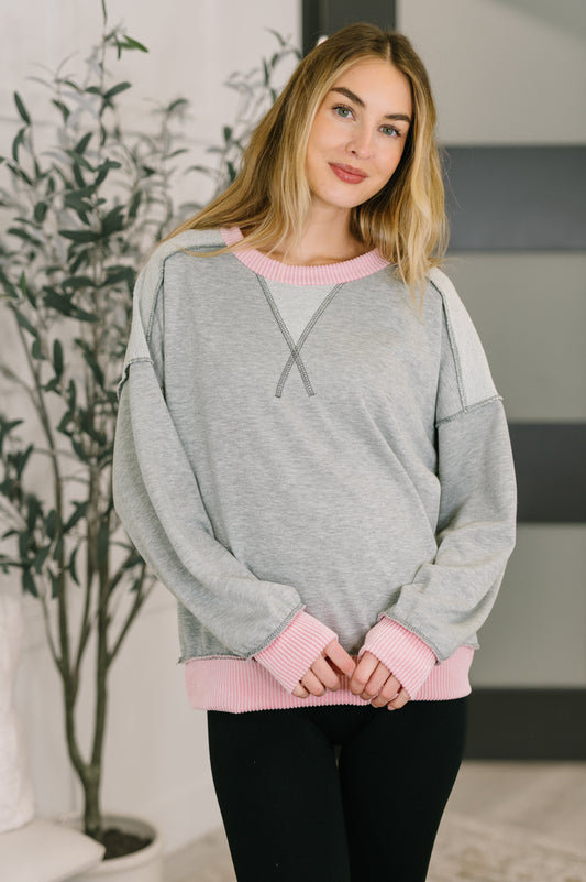 Woman wearing a gray and pink sweater standing indoors with a plant in the background