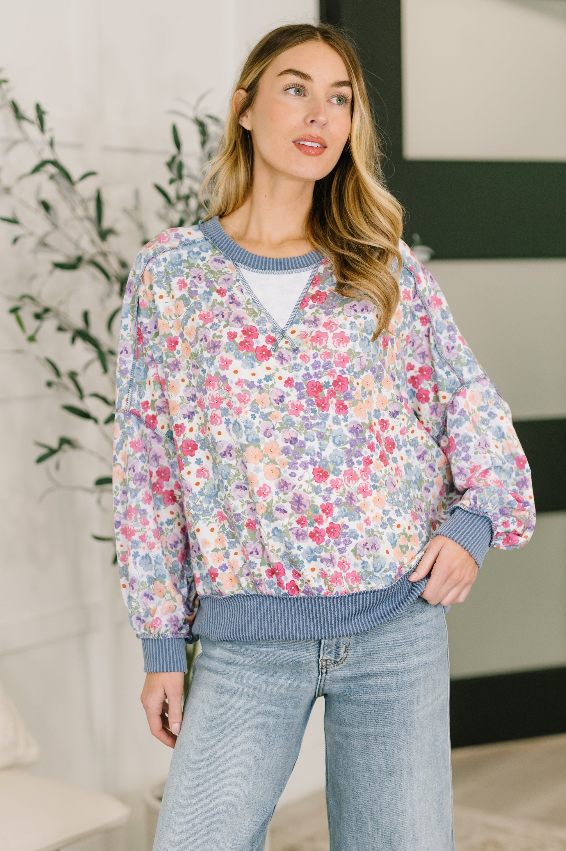 Woman wearing a floral sweater and jeans indoors with a plant in the background