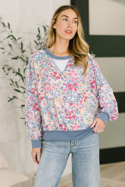 Woman wearing a floral sweater and jeans indoors with a plant in the background