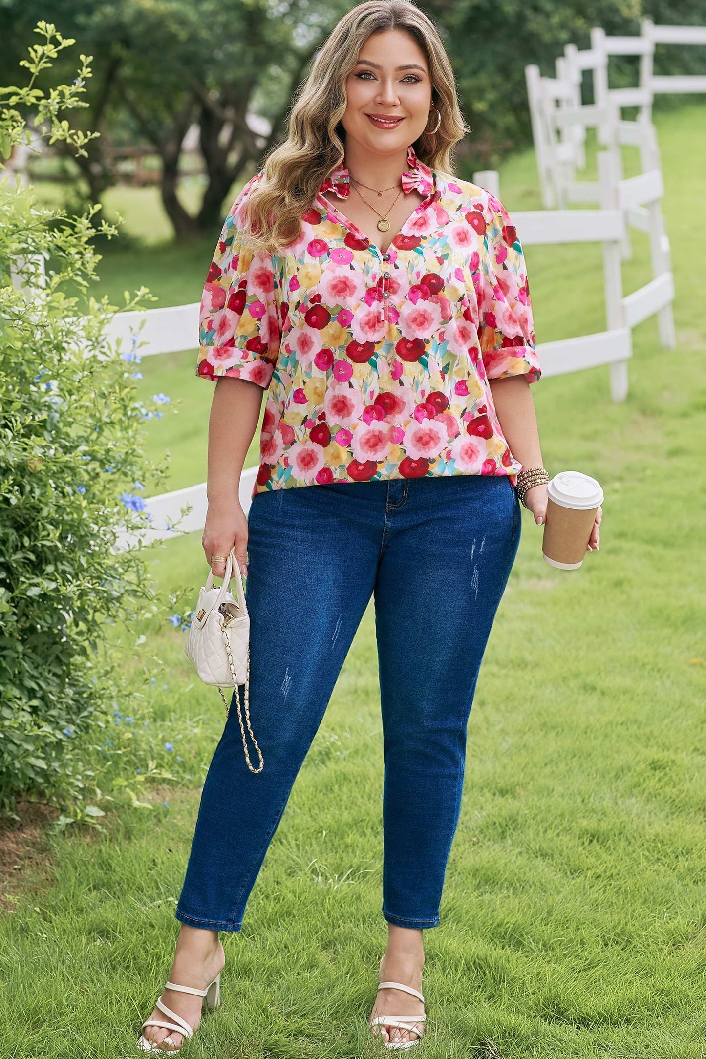 Woman in a colorful floral shirt and blue jeans standing outdoors holding a coffee cup.