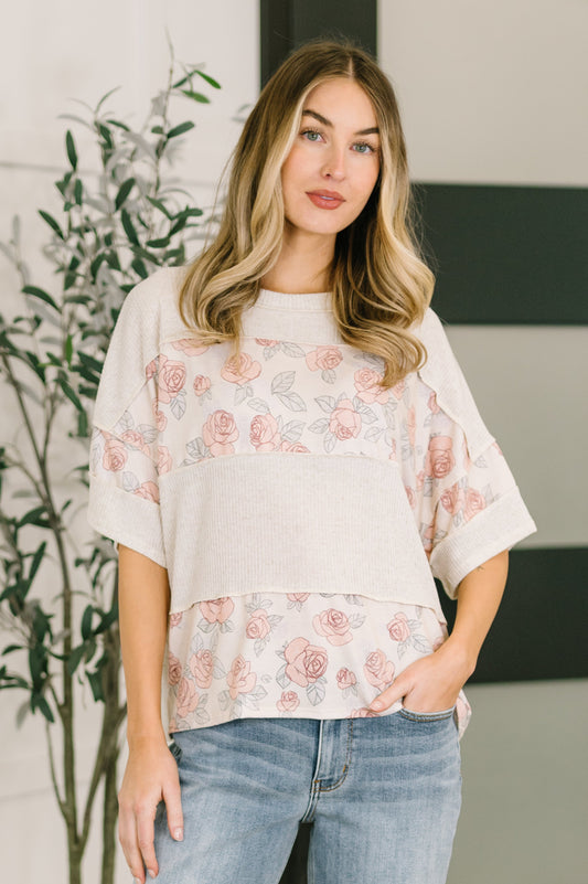 Woman wearing a floral blouse and jeans standing indoors with a plant in the background