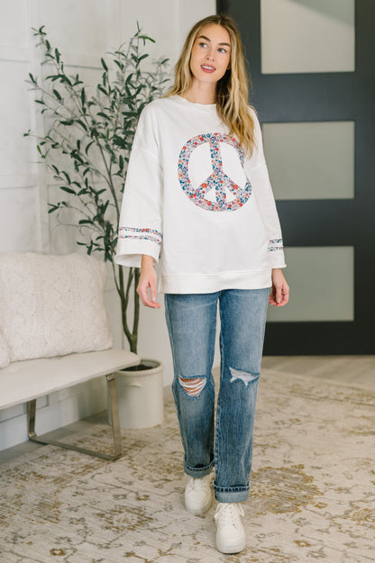 Woman wearing a white sweatshirt with a peace symbol design in a living room.